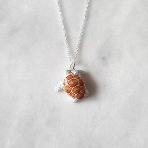 May include: A silver chain necklace with a small turtle pendant. The turtle is made of white metal with a brown and orange shell.