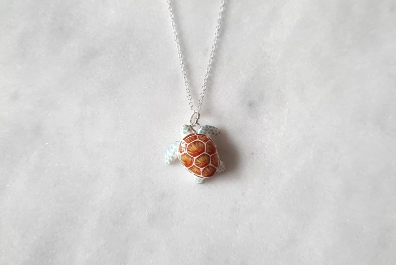 May include: A silver chain necklace with a small turtle pendant. The turtle is made of white metal with a brown and orange shell.