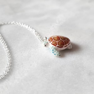 May include: A silver chain necklace with a white and brown turtle pendant. The turtle has a detailed shell with brown and orange markings and blue accents.