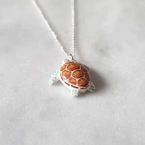 May include: A silver chain necklace with a ceramic turtle pendant. The turtle is painted with brown, orange, and green details.