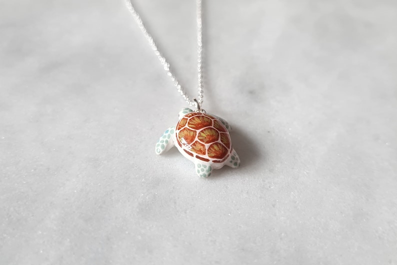 May include: A silver chain necklace with a ceramic turtle pendant. The turtle is painted with brown, orange, and green details.