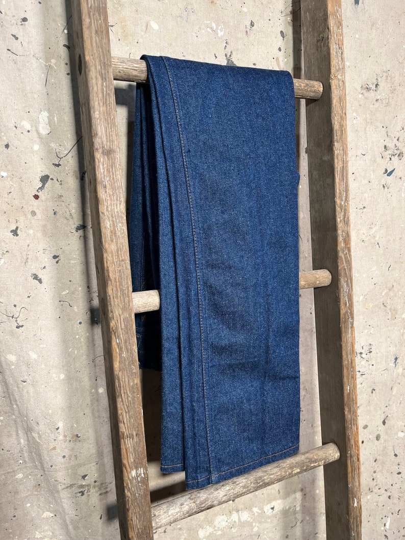 Puede incluir: Un par de pantalones vaqueros de color azul oscuro colgados de una escalera de madera.