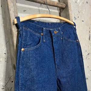 May include: A pair of dark blue denim jeans hanging on a wooden hanger. The jeans have a classic five-pocket style and a straight leg.