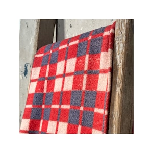 Puede incluir: Una manta a cuadros rojos, blancos y azules, colgada sobre una escalera de madera. La manta presenta un patrón repetitivo de cuadrados rojos, blancos y azules. La manta está hecha de un material suave y texturizado.