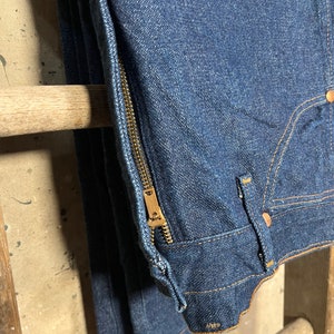 Puede incluir: Un par de pantalones vaqueros de mezclilla azul oscuro con una cremallera dorada en la costura lateral.