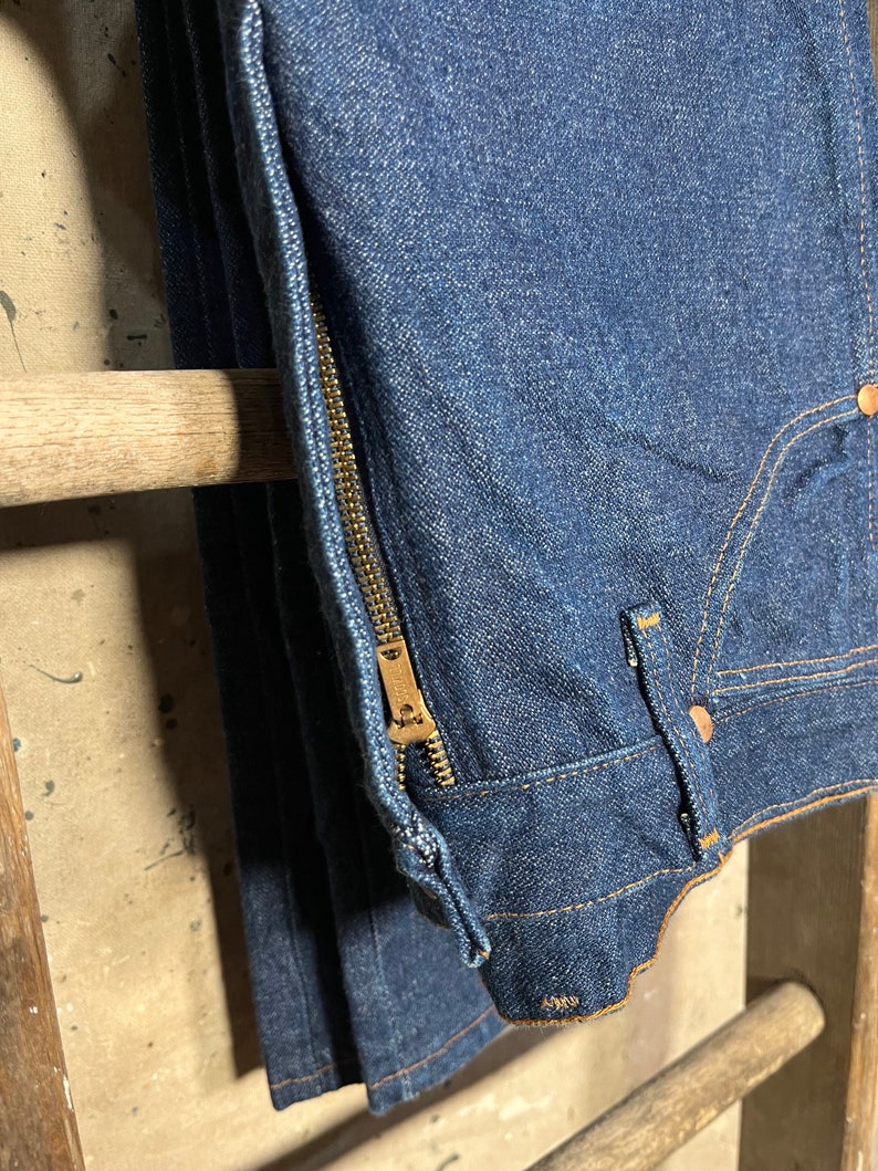 Puede incluir: Un par de pantalones vaqueros de mezclilla azul oscuro con una cremallera dorada en la costura lateral.