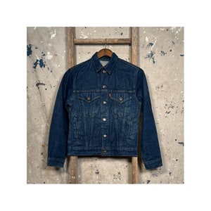 May include: A dark blue denim jacket with a button closure and a red Levi's logo on the pocket.