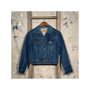 May include: A blue denim jacket with a button closure and two front pockets. The jacket has a classic style and is made of a durable material.