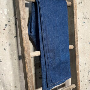 Puede incluir: Un par de pantalones vaqueros de mezclilla azul oscuro colgados en una escalera de madera.