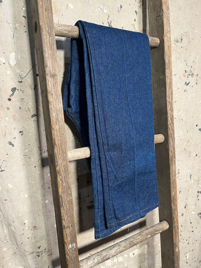 Puede incluir: Un par de pantalones vaqueros de mezclilla azul oscuro colgados en una escalera de madera.