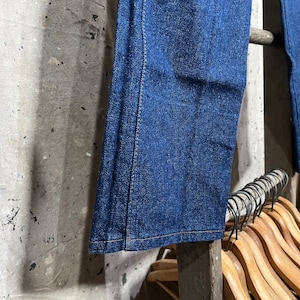 May include: A pair of dark blue denim jeans with a straight leg, hanging on a wooden rack.
