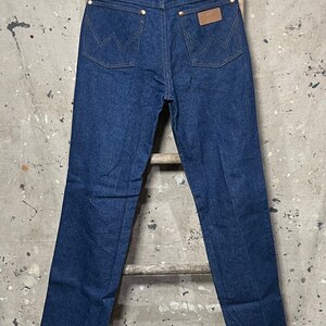 May include: A pair of dark blue denim jeans with a brown leather patch on the back pocket that says "Wrangler".