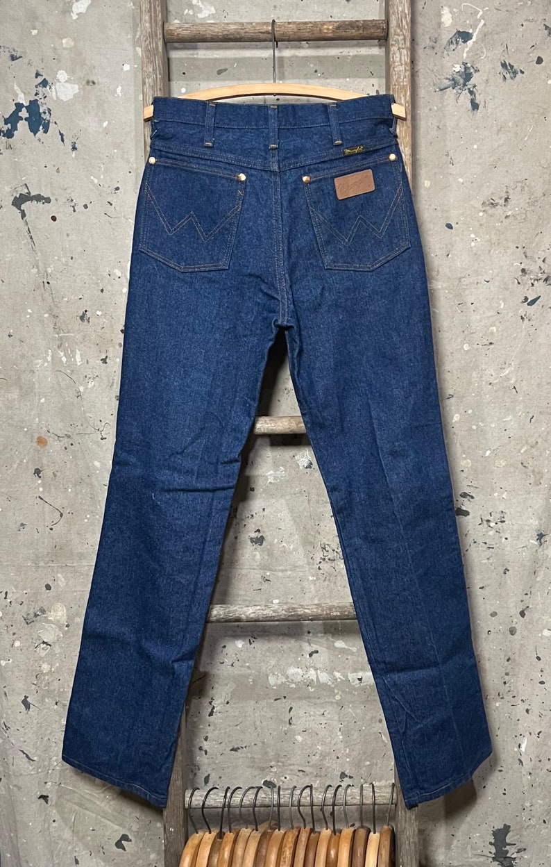 May include: A pair of dark blue denim jeans with a brown leather patch on the back pocket that says "Wrangler".