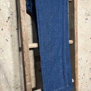 Puede incluir: Un par de pantalones vaqueros de mezclilla azul oscuro colgados en una escalera de madera.
