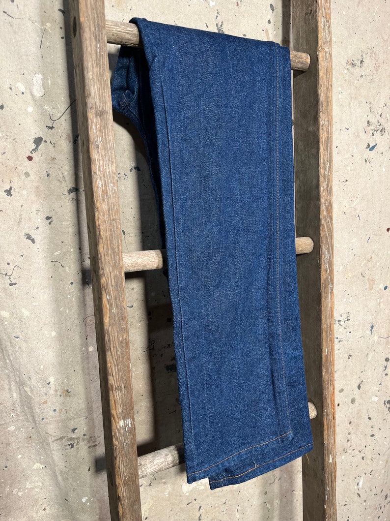 Puede incluir: Un par de pantalones vaqueros de mezclilla azul oscuro colgados en una escalera de madera.