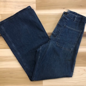 May include: A pair of dark blue denim jeans with a wide leg and a high waist. The jeans have a large patch pocket on each side and a button fly.