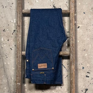 Puede incluir: Un par de pantalones vaqueros de mezclilla azul oscuro con un parche de cuero marr&oacute;n que dice "Wrangler" en el bolsillo trasero.