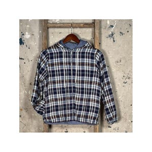 May include: A navy blue, white, and burgundy plaid hooded jacket hangs on a wooden hanger. The jacket has a full zip and a light blue hood lining. The background is a distressed, textured wall with a wooden ladder.