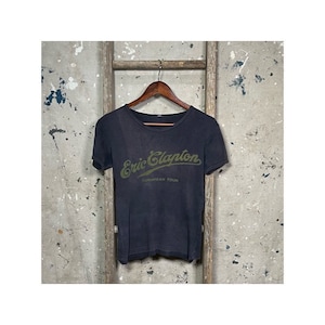 May include: A dark gray t-shirt with a green and white graphic print of "Eric Clapton" and "European Tour".