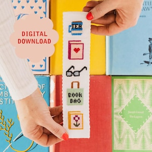 May include: White cross-stitch bookmark with five colorful designs: a cup of tea, a book with a heart, glasses, a book bag, and a flower. The bookmark is held by a hand against a background of colorful books.