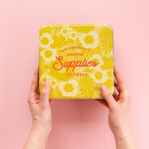 May include: A yellow metal tin with a floral pattern and the text "Universally Useful Supplies and Tools".