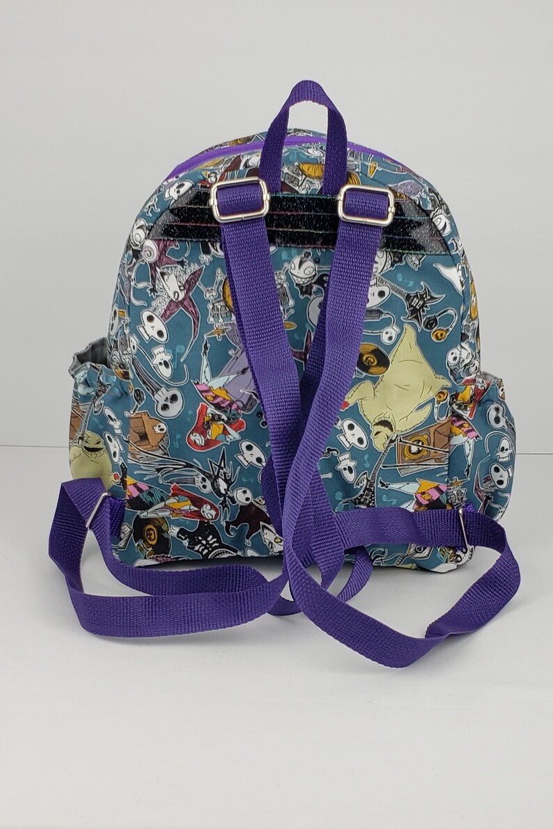 May include: A purple and blue backpack with a Nightmare Before Christmas print. The backpack has a large compartment and two adjustable straps.