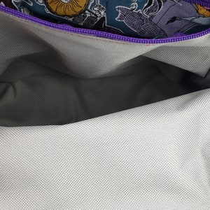 May include: The inside of a purple zippered bag with a gray fabric lining. The zipper is open and the lining is visible. The bag is decorated with a colorful print of characters from the Nightmare Before Christmas.