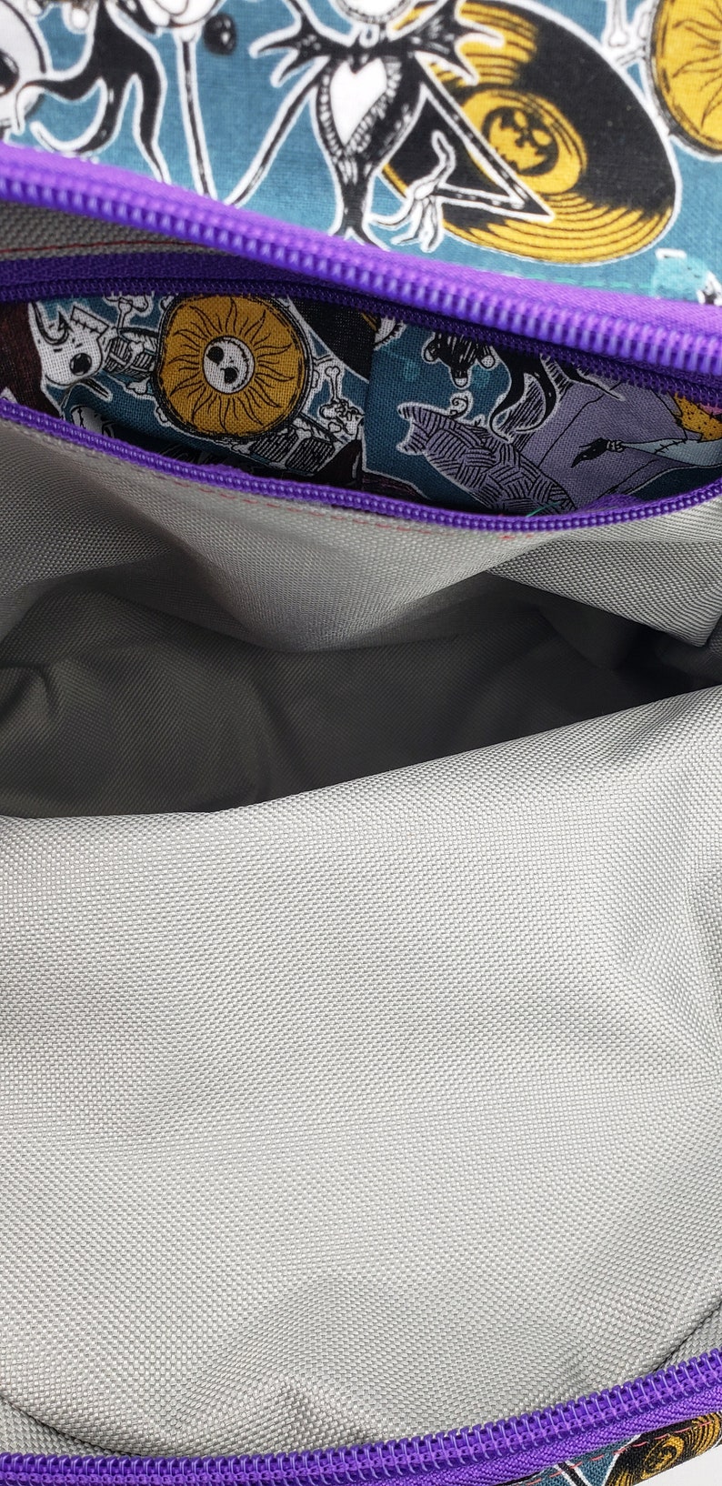 May include: The inside of a purple zippered bag with a gray fabric lining. The zipper is open and the lining is visible. The bag is decorated with a colorful print of characters from the Nightmare Before Christmas.