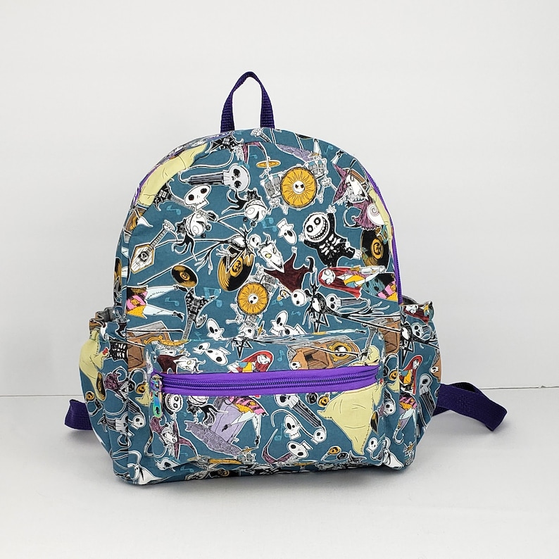 May include: A blue and purple backpack with a Nightmare Before Christmas print. The backpack features characters from the movie, including Jack Skellington, Sally, and Oogie Boogie.