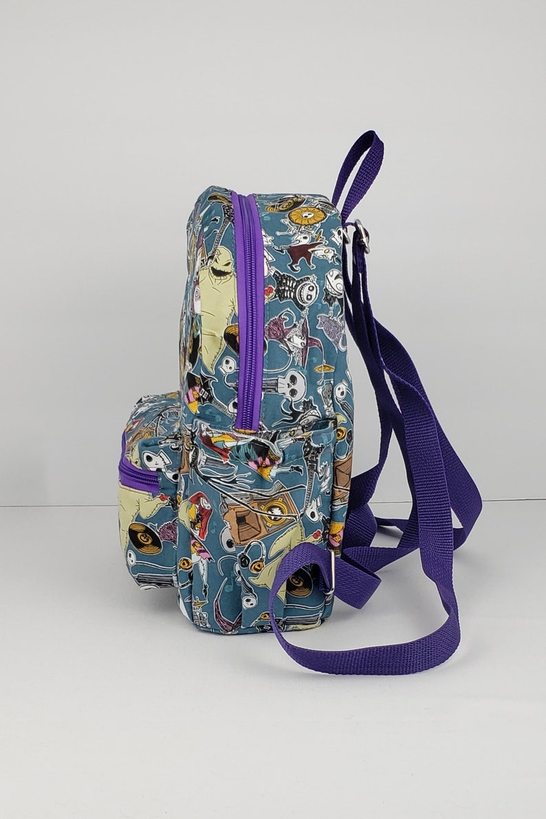 May include: A small blue and purple backpack with a print of characters from the Nightmare Before Christmas. The backpack has a zippered pocket on the front and adjustable straps.