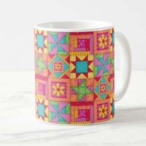 May include: A white ceramic mug with a colorful patchwork design. The pattern features squares and triangles in shades of pink, red, orange, yellow, green, and blue. The design includes small yellow flowers.