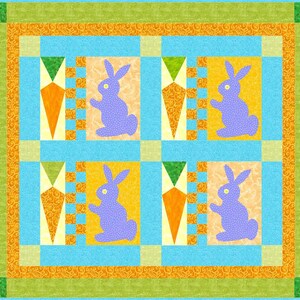 May include: A quilt with a blue background and a patchwork design. The quilt features four purple bunnies and four orange carrots. The quilt is surrounded by a green and orange border.