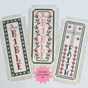 May include: Three counted cross stitch bookmark kits. The first bookmark features the words "The Bible" in pink lettering with a green border. The second bookmark features the words "The Bible" in pink lettering with a floral design. The third bookmark features the word "Faith" in blue lettering with a cross design.