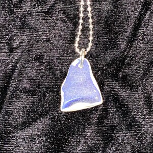 May include: A silver chain necklace with a blue and white glass pendant. The pendant is shaped like a teardrop and has a smooth, polished surface.