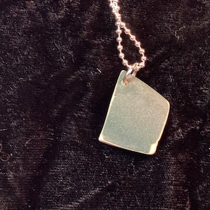 May include: A silver chain necklace with a silver, rectangular pendant. The pendant is a flat, smooth surface.