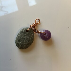 May include: A copper wire wrapped around a small grey stone with a purple glass bead attached.