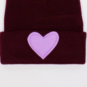 May include: A burgundy knit beanie with a purple heart sewn on the front.