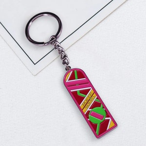May include: A pink and red metal keychain shaped like a hoverboard, with the words "HOVER BOARD" in yellow. The keychain has a silver chain and ring.