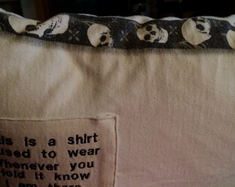 May include: A white pillow with a black skull print border. The pillow has a pocket with the text "This is a shirt I used to wear Whenever you Hold It know I am there" printed on it.