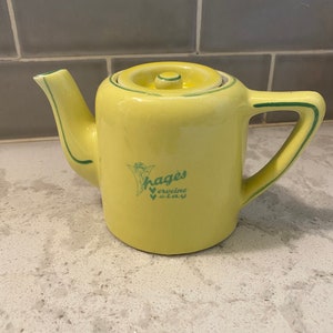 May include: Yellow ceramic teapot with a green lid and green trim. The teapot has a green image of a flower and the text "Hages Verveine Clay" on the side.