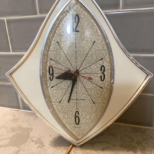 May include: A white diamond-shaped wall clock with a silver trim and a white face with a gray swirl pattern. The clock face has black numbers and black hands. The clock says "General Electric" and "Made in U.S.A."