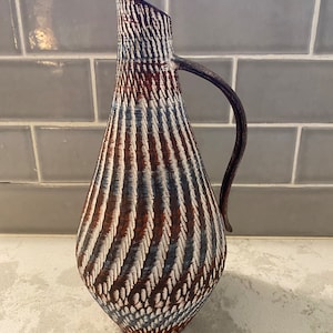 May include: A brown and white ceramic pitcher with a swirling pattern. The pitcher has a handle and a rounded body.