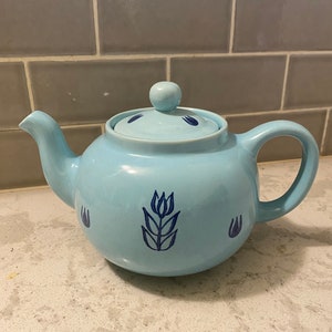 May include: A light blue teapot with a floral design. The teapot has a lid and a spout. The floral design is in blue and white.