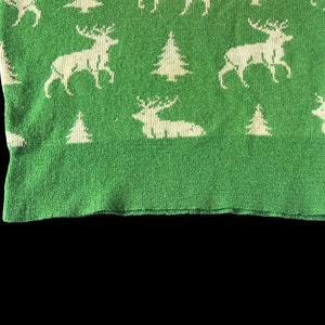 May include: Green knitted fabric with a white pattern of stylized reindeer and pine trees.