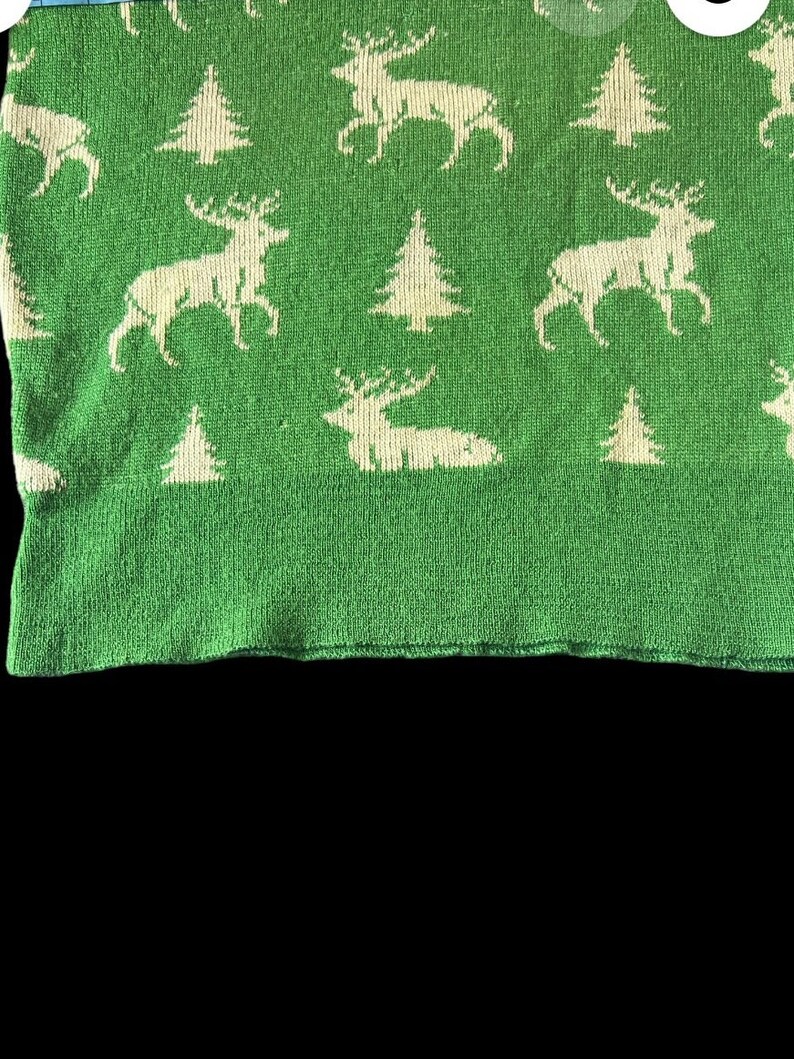May include: Green knitted fabric with a white pattern of stylized reindeer and pine trees.