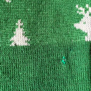 May include: Green knitted fabric with a white knitted design of a Christmas tree and a reindeer. The fabric has a small hole in it.