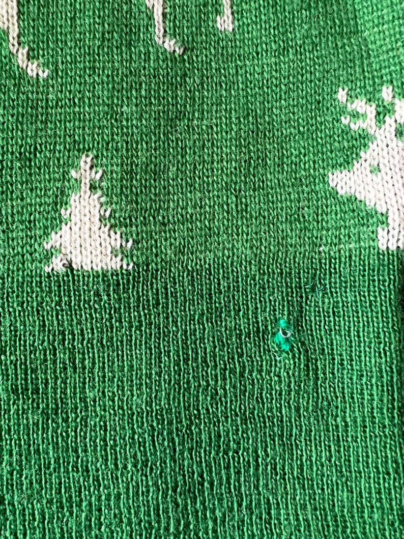 May include: Green knitted fabric with a white knitted design of a Christmas tree and a reindeer. The fabric has a small hole in it.