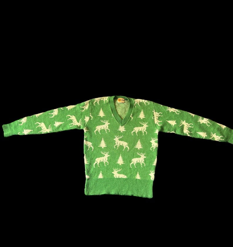 May include: A green sweater with a white reindeer pattern. The sweater has a V-neck and long sleeves.