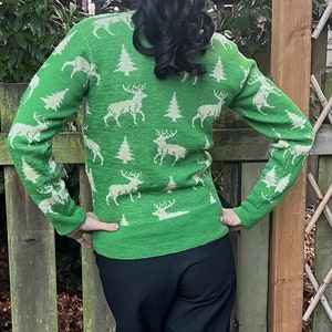May include: A green sweater with a white reindeer and Christmas tree pattern. The sweater is long-sleeved and has a crew neck.
