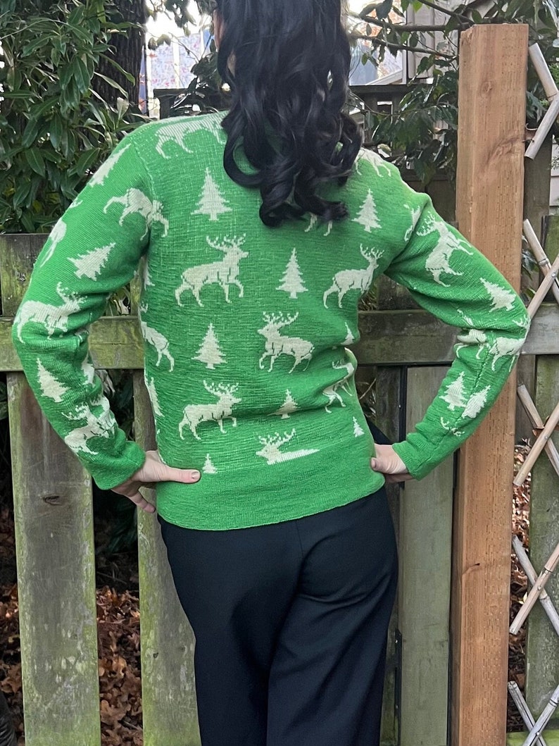May include: A green sweater with a white reindeer and Christmas tree pattern. The sweater is long-sleeved and has a crew neck.
